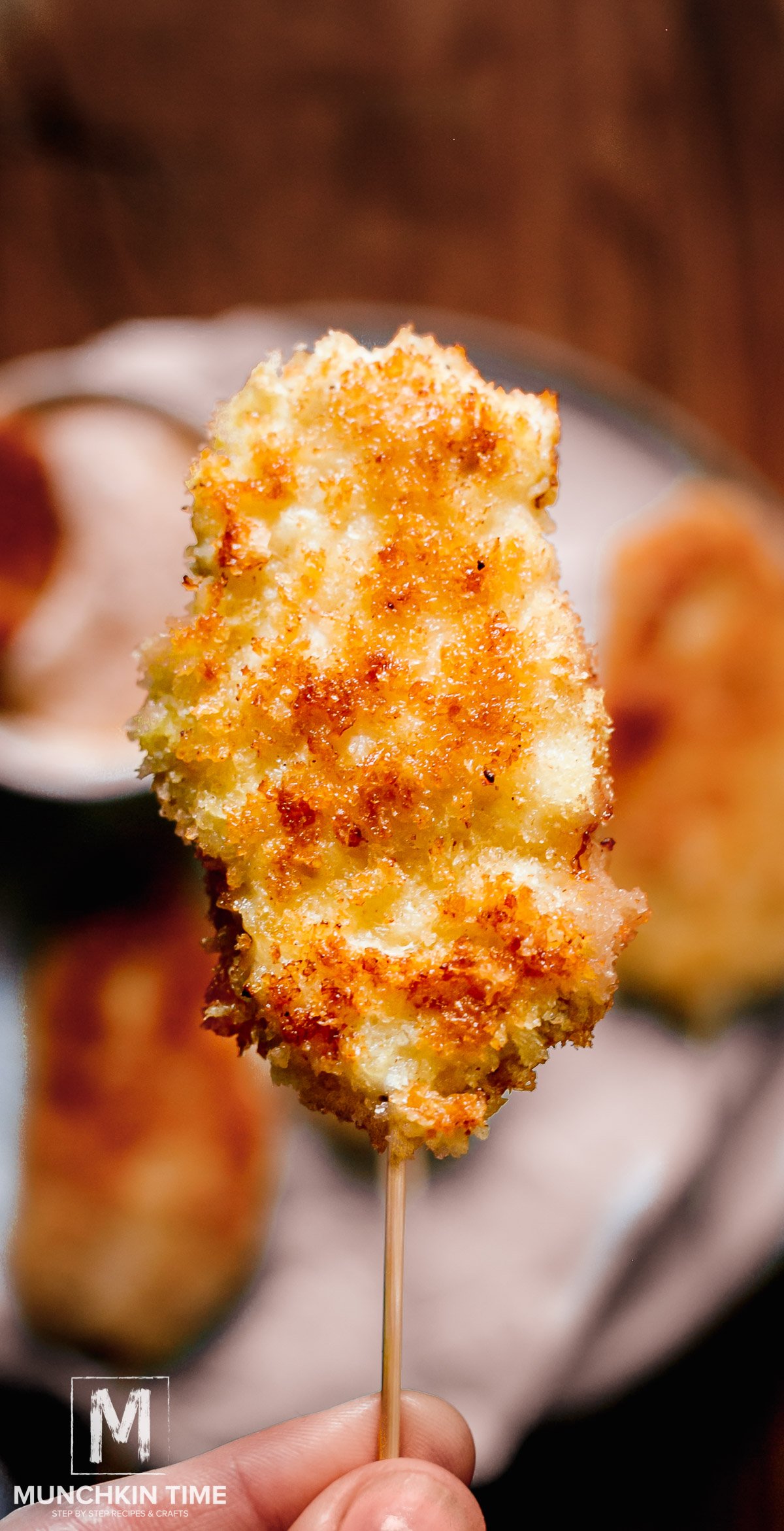 A hand holding chicken on a stick above the plate. 