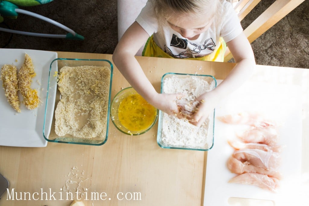 Hand dusting chicken strips in flour. 
