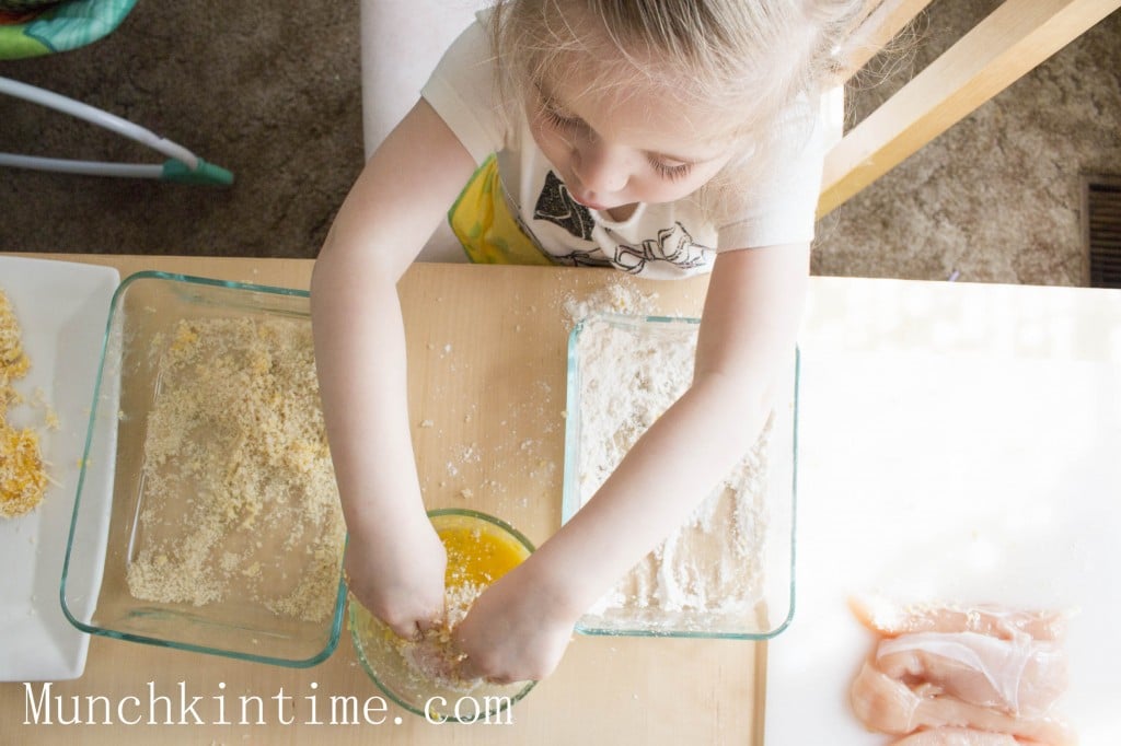 A picture of a hands coating chicken strips in egg wash. 