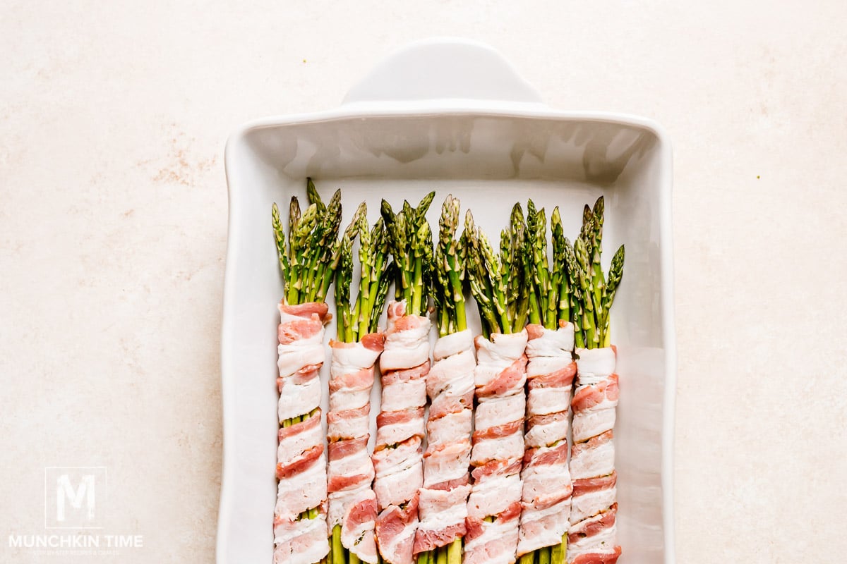 Asparagus bundles wrapped in bacon inside the white casserole dish.