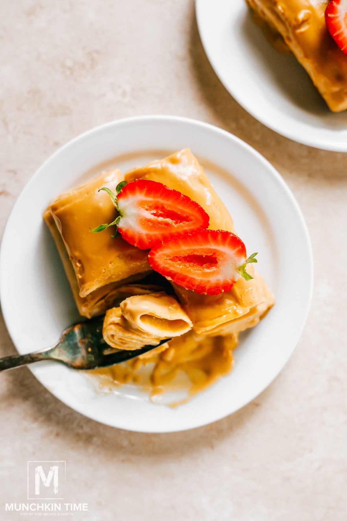 Baked crepes with cream and sliced strawberries on top, on a white plate. Final shot of easy crepe recipe.