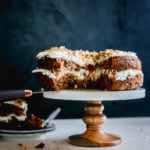 Best Carrot Cake Recipe From Scratch - a cut open carrot cake on a cake stand. Another slice on a plate next to the carrot cake.