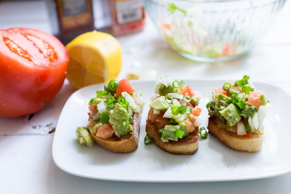  Avocado Garlic Tomato Bruschetta on a plate next to big tomato and lemon.