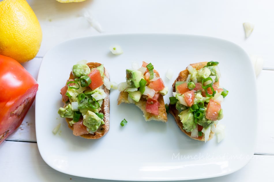 3 tomato avocado bruschetta on the plate, one is eaten half way. 