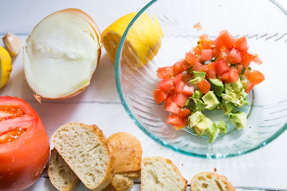 Sliced avocado inside the mixing bowl with cubed tomatoes.