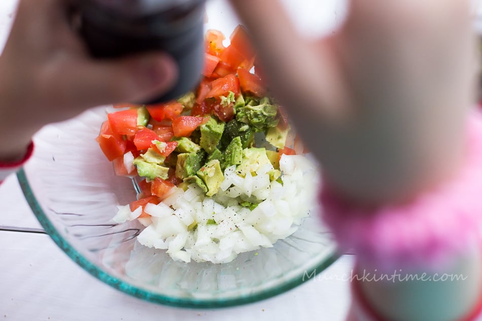 On this picture hands holding salt shaker seasoning tomato avocado mixture for tomato bruschetta.