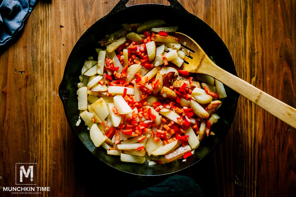 Chopped red bell pepper inside the skillet with hash brown potatoes.
