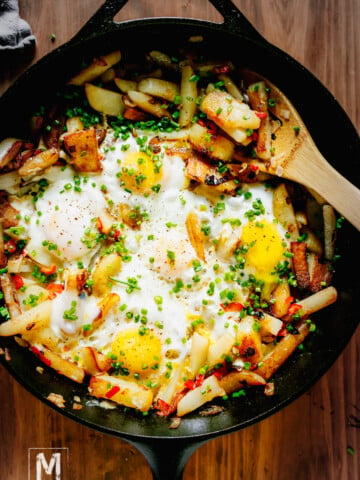 Potato Hash with Eggs inside the cast iron skillet, garnished with chives and black pepper.