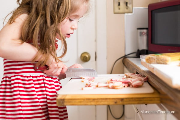 A girl chopping bacon into tiny pieces.