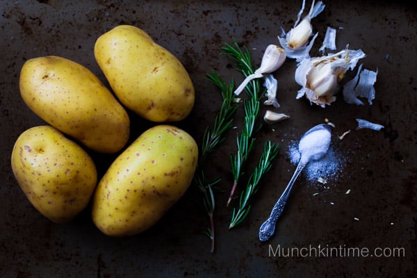 Unpeeled potatoes with garlic and rosemary on the table.