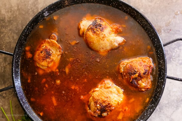 Paella skillet filled with chicken broth, chicken, tomato, and saffron.