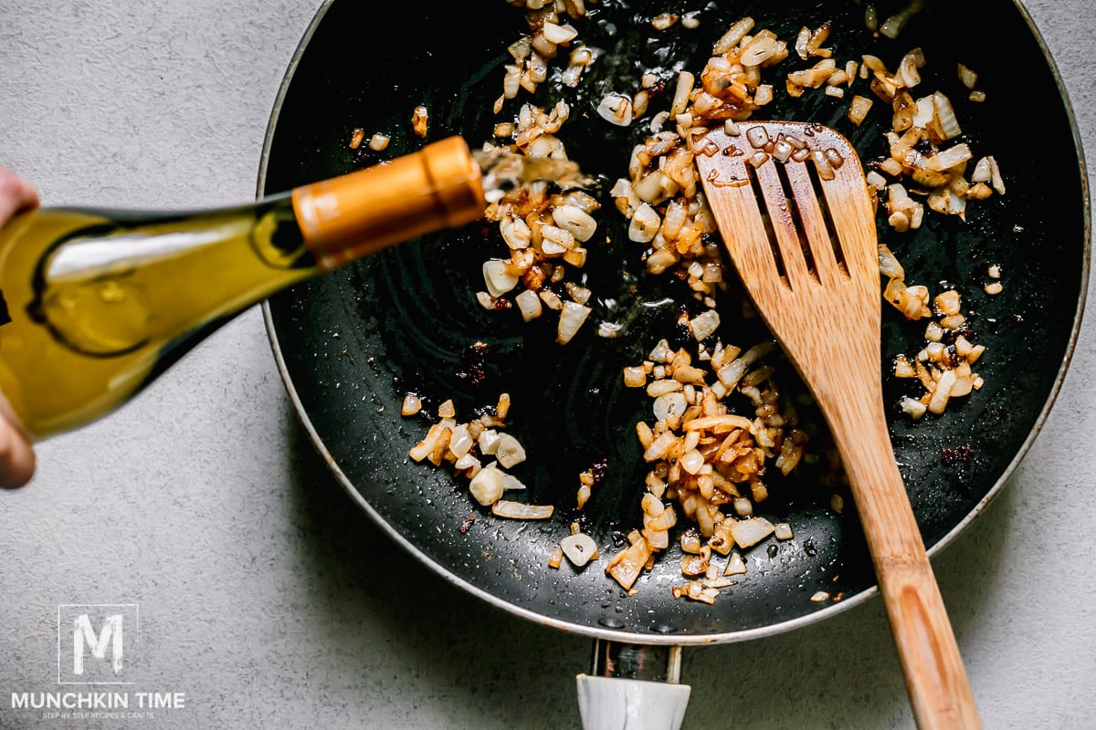 White white wine pouring out into a skillet with sautéed onion and garlic.