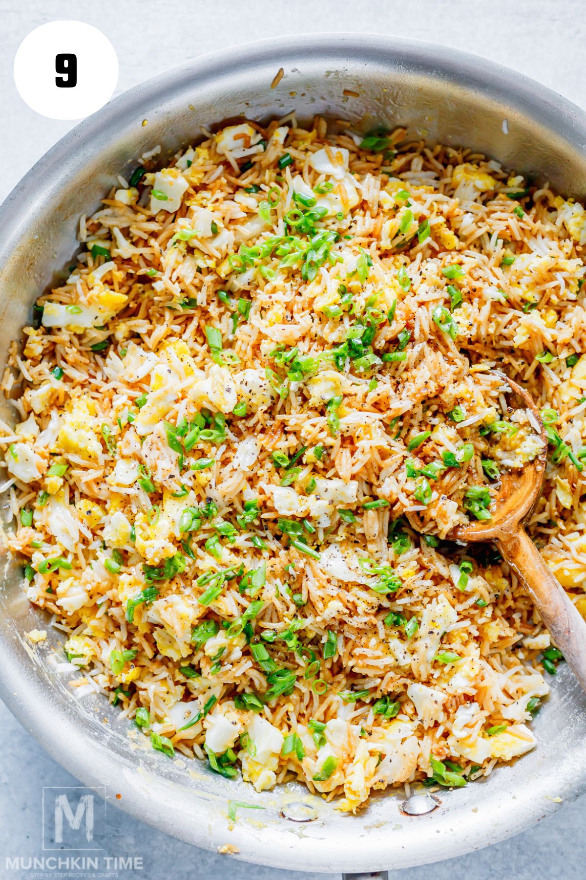 Adding scrambled eggs and green onion to the fried rice in a skillet.