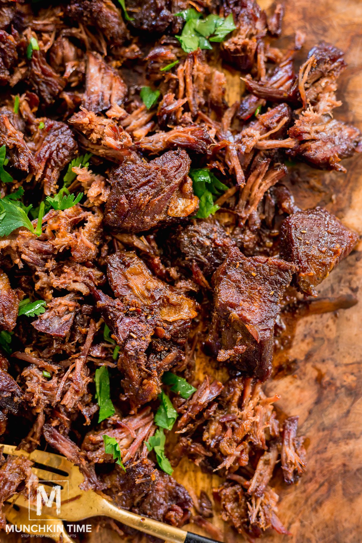 Pot roast beef shredded with 2 forks on a cutting table.