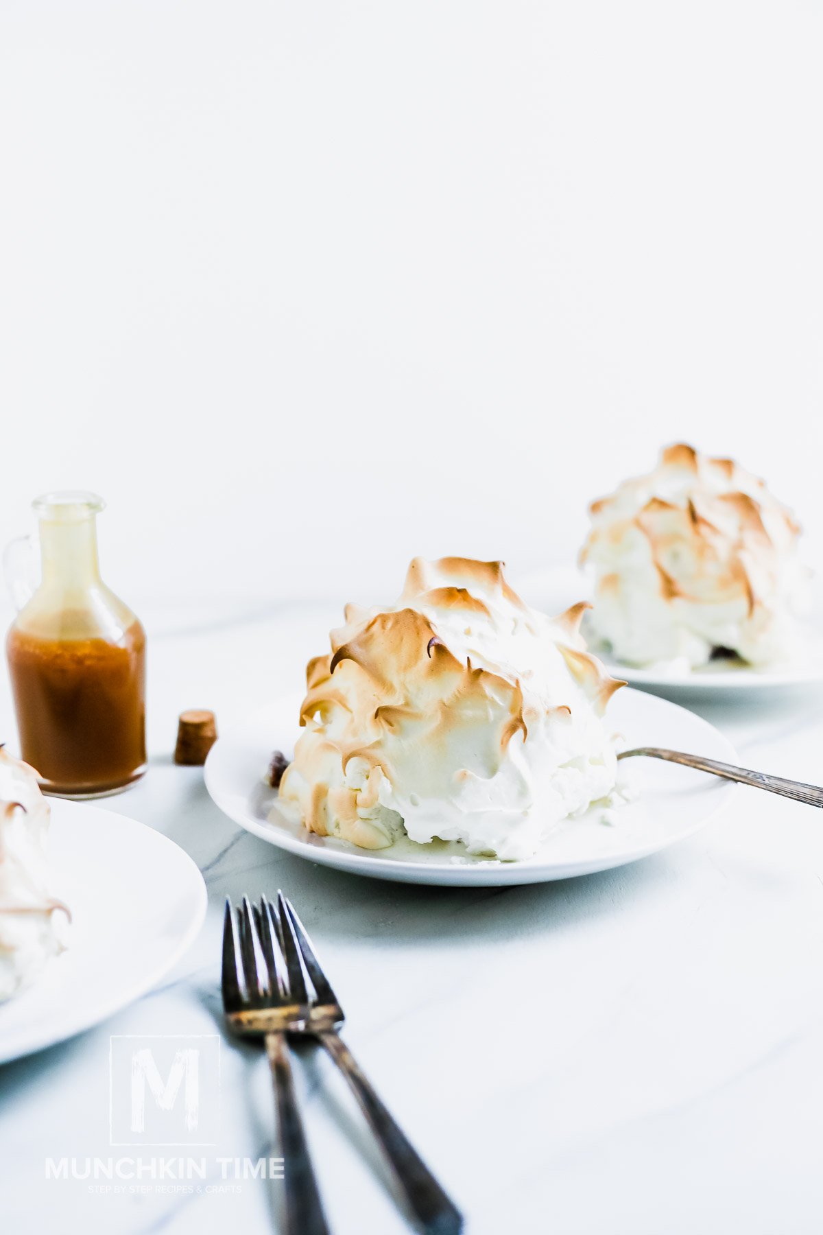 Baked Alaska cakes on a white plate with a caramel jar on a side.