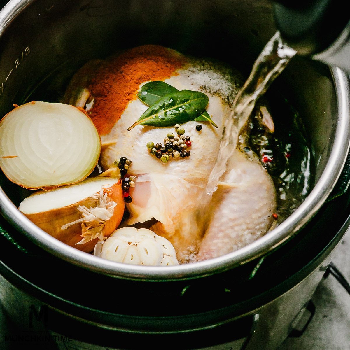 water pouring into the instant pot filled with whole chicken cut up onion, galric and spices