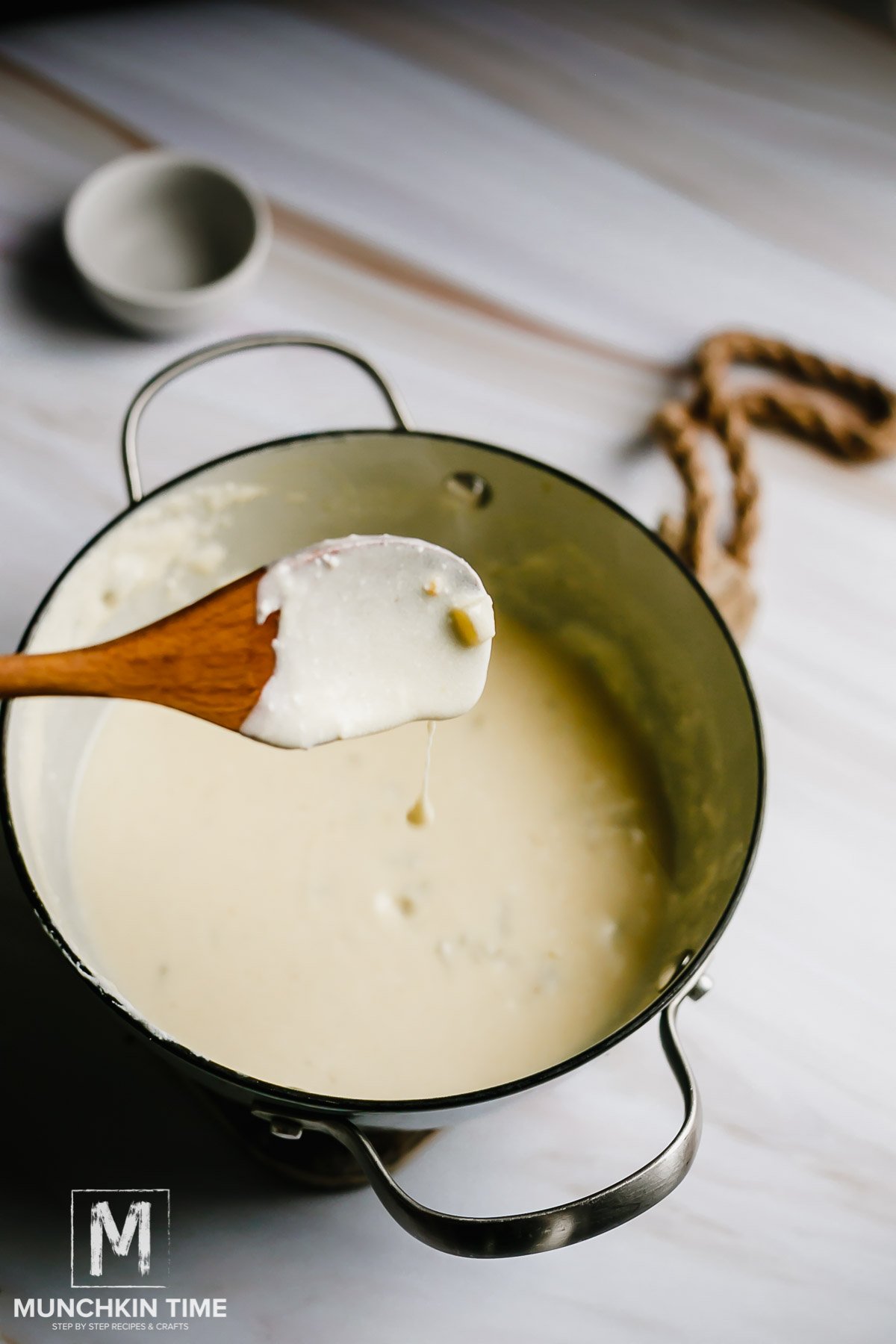 A wooden spoon dripping white Mexica sauce into the sauce pot. 