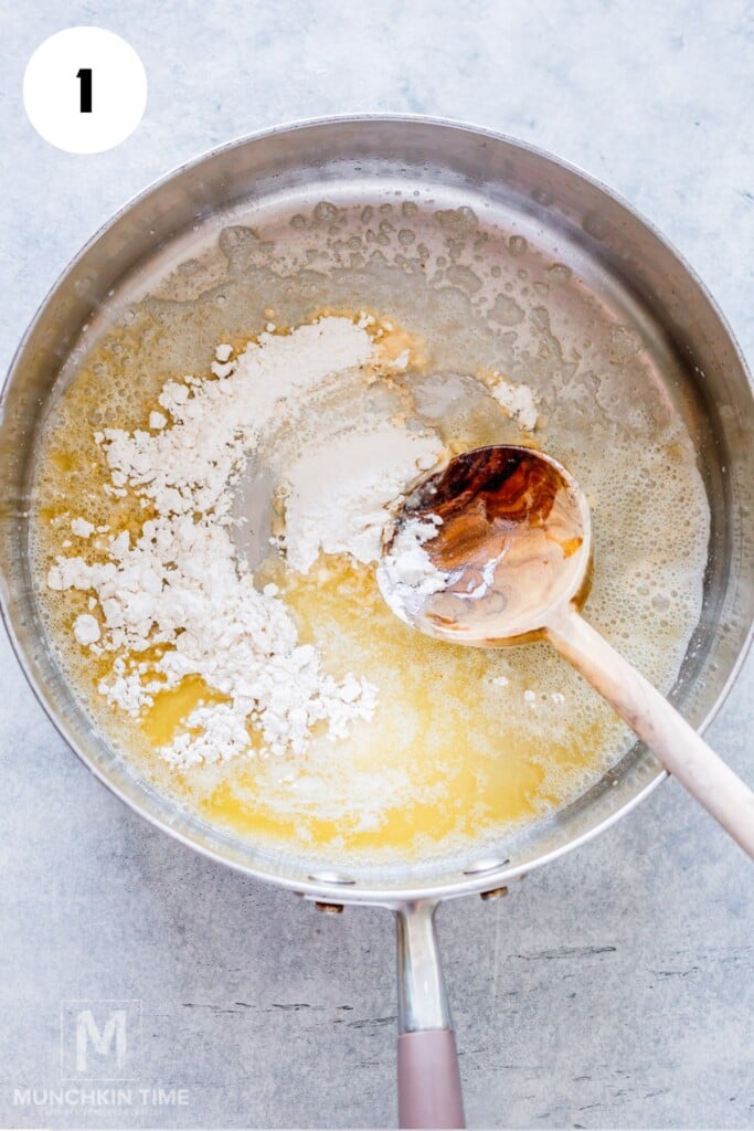 A saucepan with melted butter and flour being stirred with a wooden spoon, starting the process of making a roux.