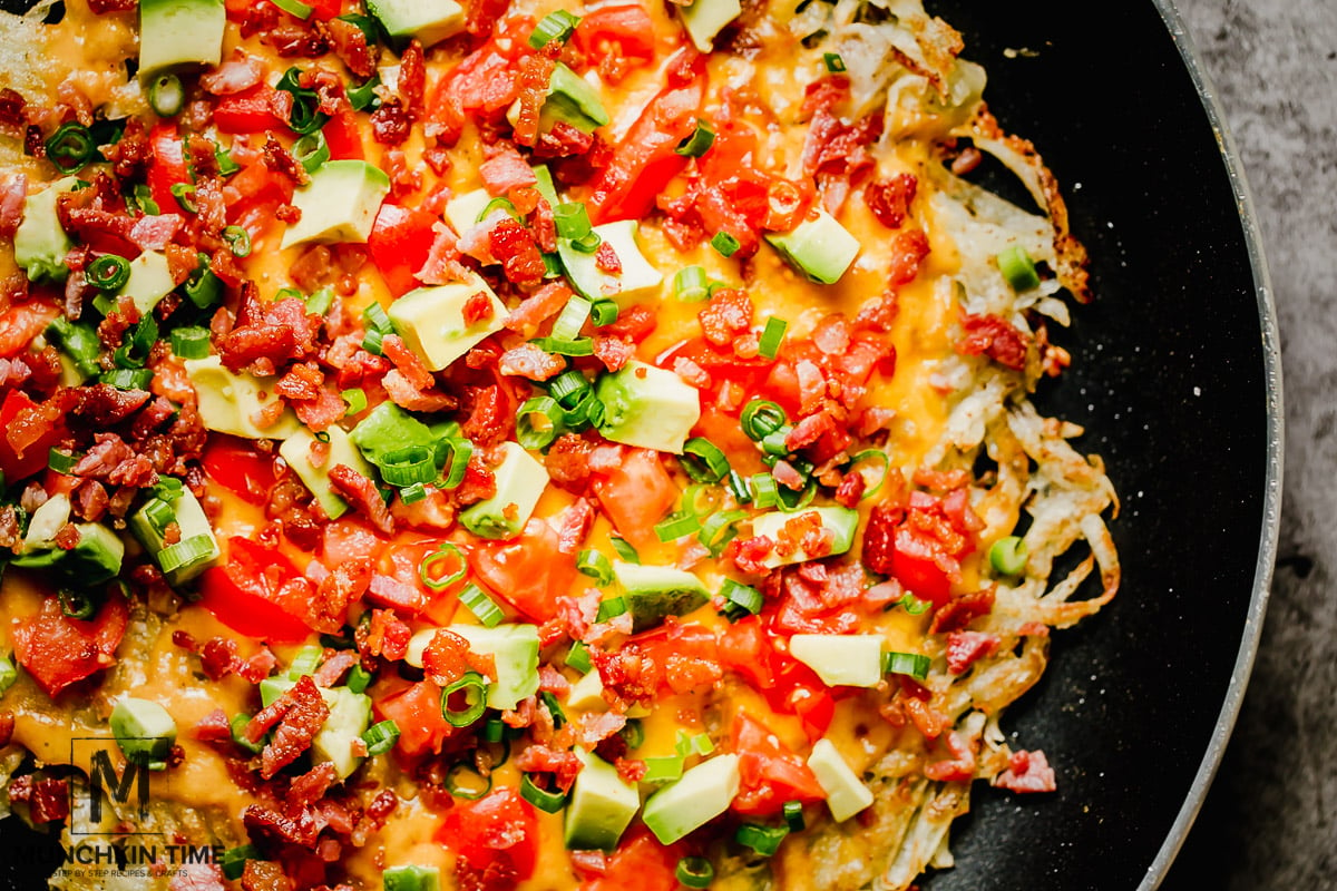 How to Make Breakfast Pizza Step 1: Cook bacon in a skillet over medium-high heat for about 5 minutes, stirring occasionally, until the bacon is crispy. Transfer the cooked crumbles to a paper towel lined plate and remove all but 1 Tablespoon of the grease from the skillet. Step 2: To the same skillet, drizzle grape seed oil (or olive oil) and add the hash brown. Use a spatula to press down the grated potato into the bottom of the skillet, making a single layer of one big hash brown. Season with salt and pepper. Step 3: Cook the hash brown over medium-high heat for 5-7, undisturbed. Once crispy and golden, carefully flip it to the other side and top with the cheddar cheese. Cook for another 5-7 minutes on the second side until golden and crispy on the bottom as well. 25-Min Cheesy Hash Browns Breakfast Pizza Recipe