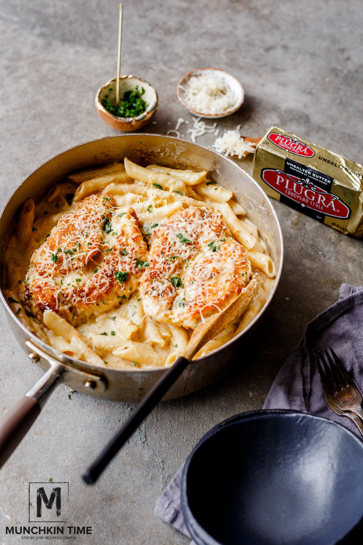Oven Baked Chicken Pasta in Buttery White Sauce inside the skillet with a wooden spoon and a plate on the side.