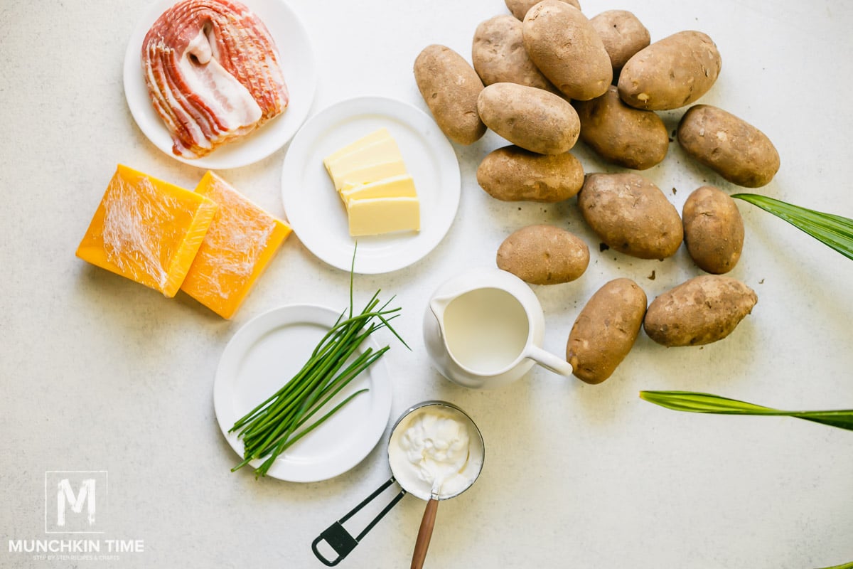 Flat lay of the ingredients for mashed potatoes, on the table laying potatoes, milk, chives, sour cream, butter, cheese and bacon.