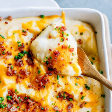 A scoop of baked mashed potatoes garnish with cheese, bacon pieces and chives.
