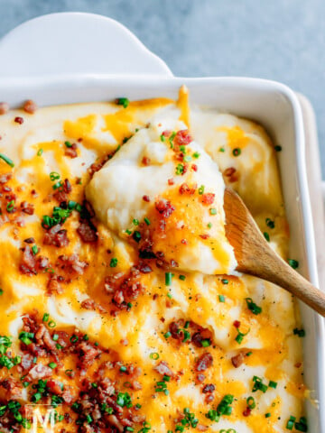 A scoop of baked mashed potatoes garnish with cheese, bacon pieces and chives.