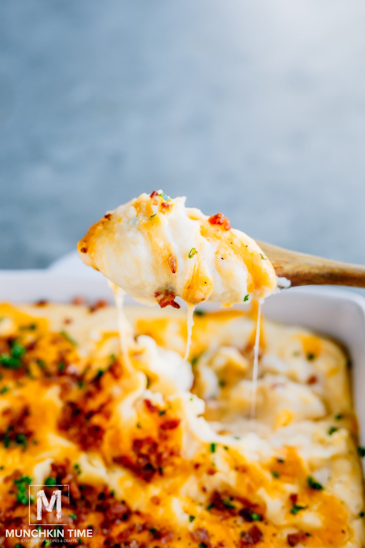 A wooden spoon pulling up a scoop of cheesy mashed potato.