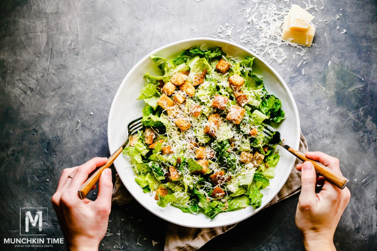 Two hands mixing Caesar salad inside the salad bowl.