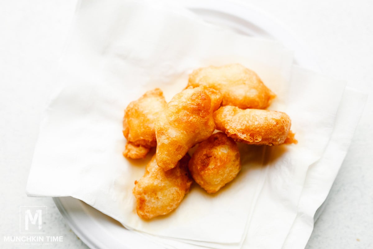 Crispy chicken pieces cooling on a plate lined with paper towel.