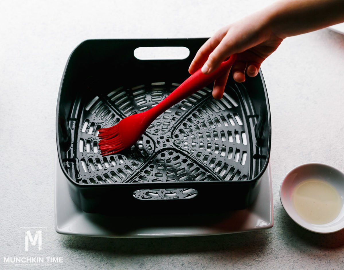 Greasing air fryer with oil before baking.