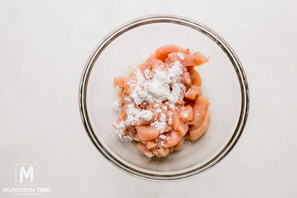 A mixing bowl with chicken pieces, cornstarch and cooking sherry.