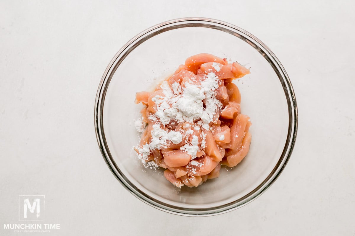 A mixing bowl with chicken pieces, cornstarch and cooking sherry.