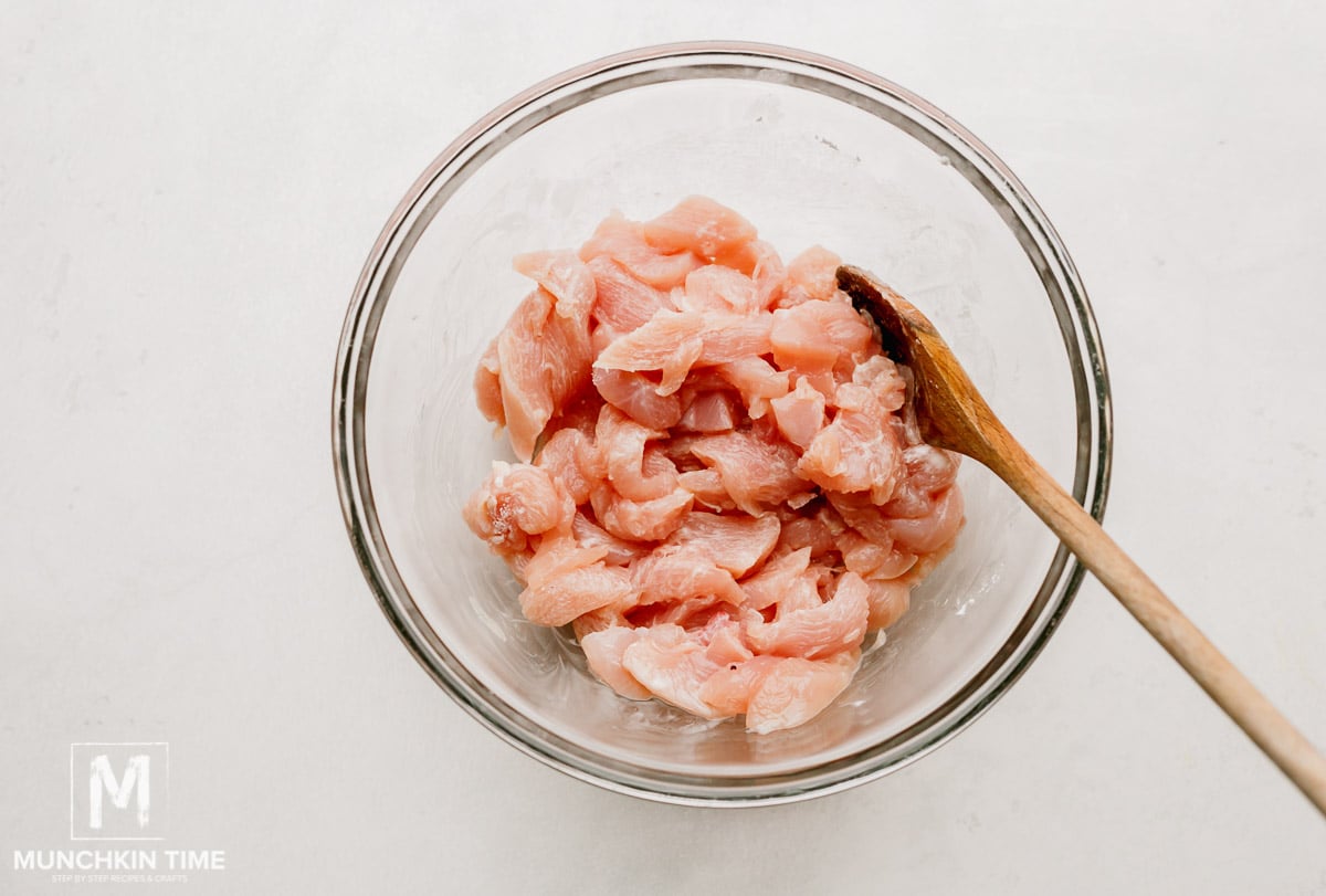 A mixing bowl with chicken pieces, cornstarch and cooking sherry, mixed.