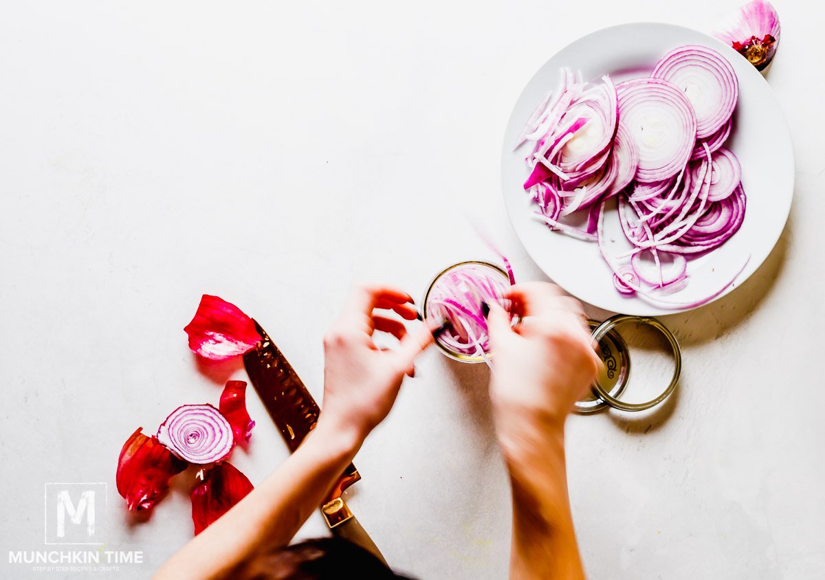 Sliced red onion being placed into a glass jar.