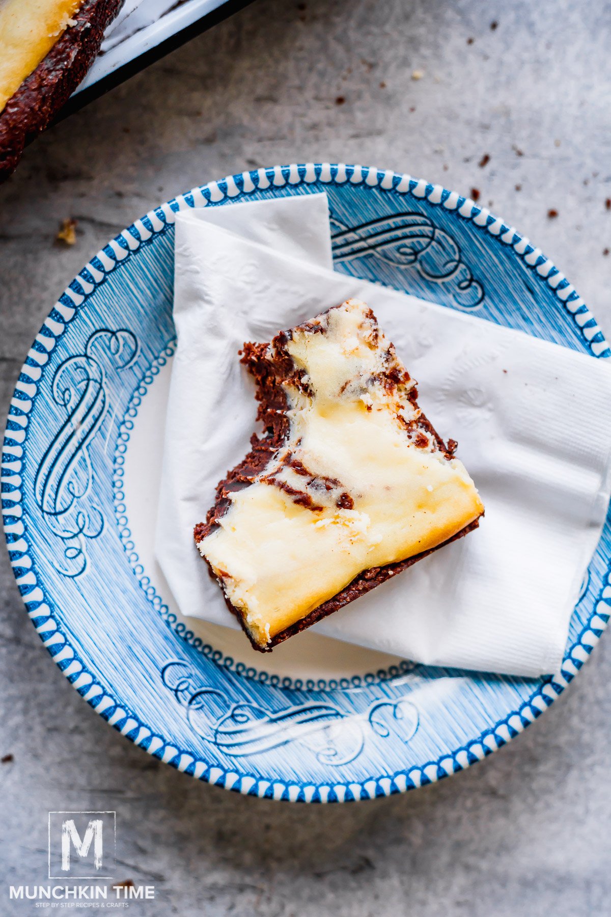 a plate with a napkin and a bitten Cheesecake Chocolate Brownie.