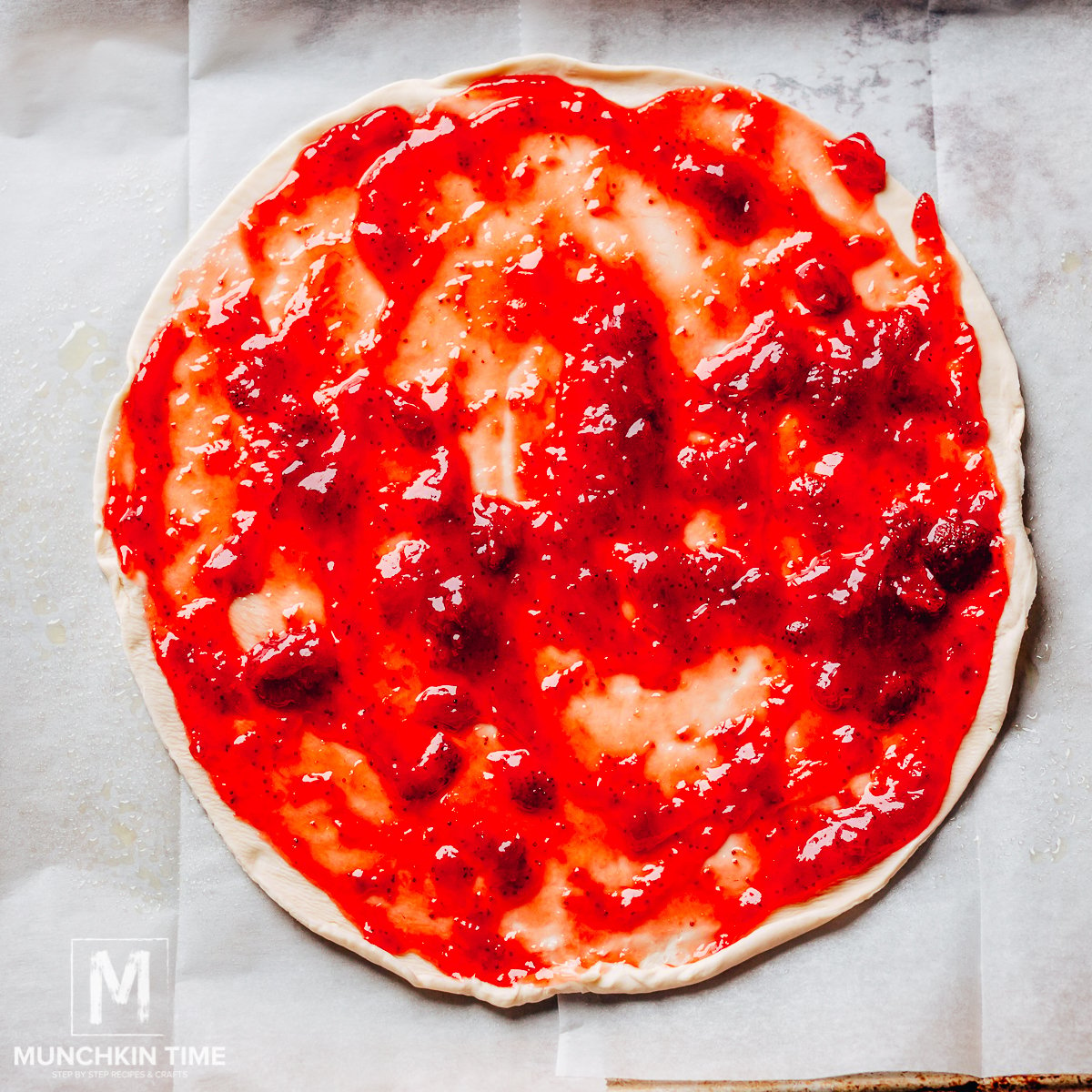 Strawberry jam evenly spread over the dough on a parchment paper.