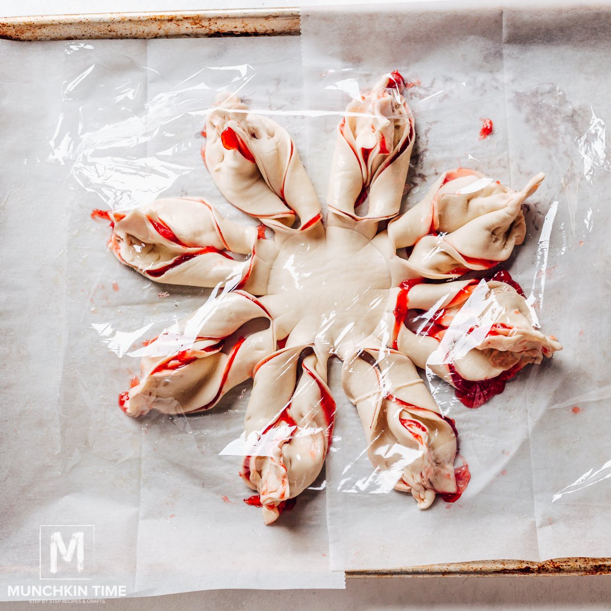 Snowflake pastry rising under plastic food wrap.