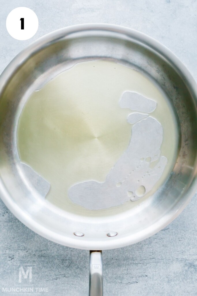 A stainless steel frying pan with a thin layer of oil on the bottom, placed on a light-colored surface.