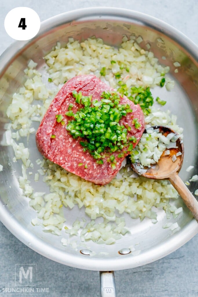 Ground beef, chopped onions, and diced green peppers in a skillet, being stirred with a wooden spoon.