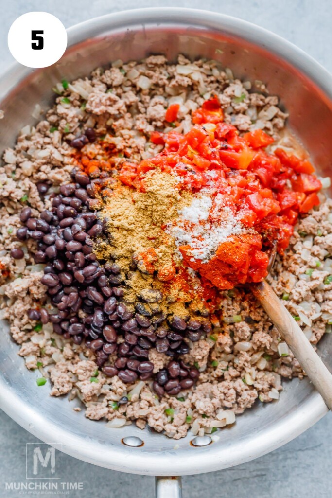 Ground meat, black beans, diced tomatoes, onions, and spices cooking in a skillet, being mixed with a wooden spoon.