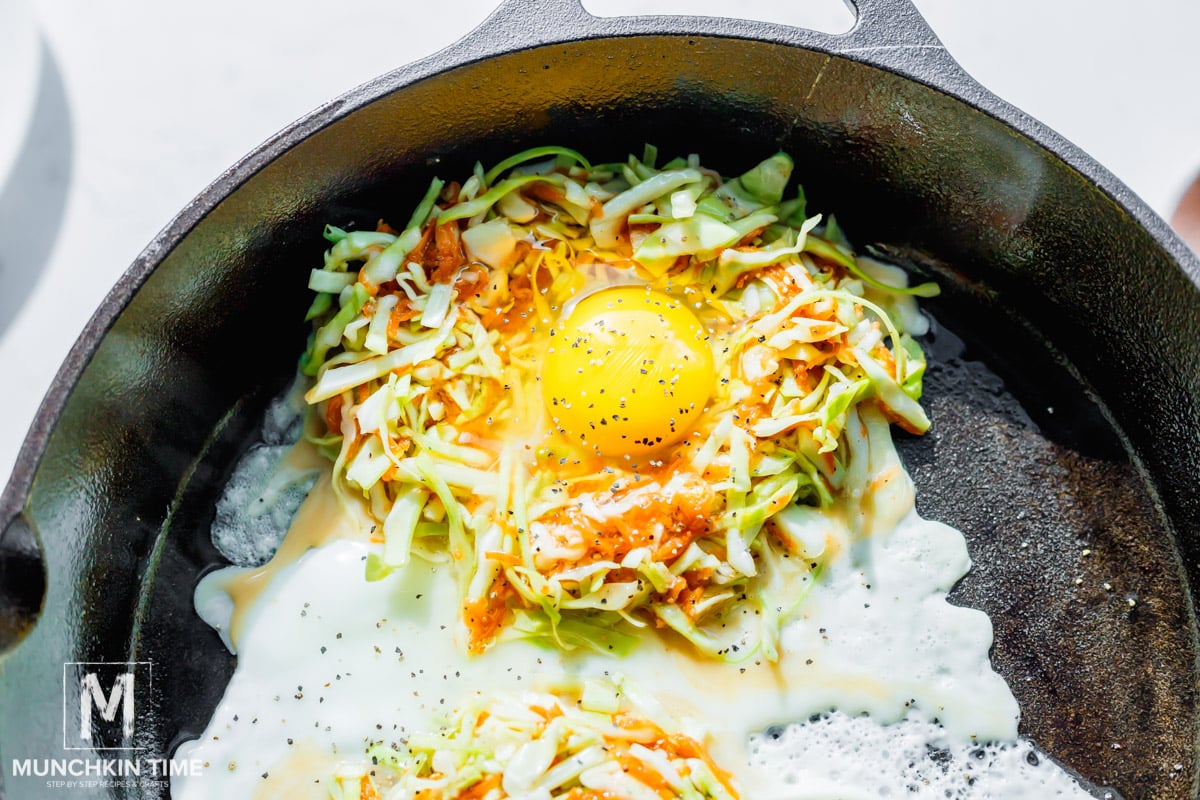 cooking eggs in a skillet on a bed of cabbage and carrots