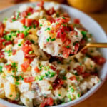 A bowl of Creamy Dill Pickle Potato Salad garnished with bacon pieces and chives.