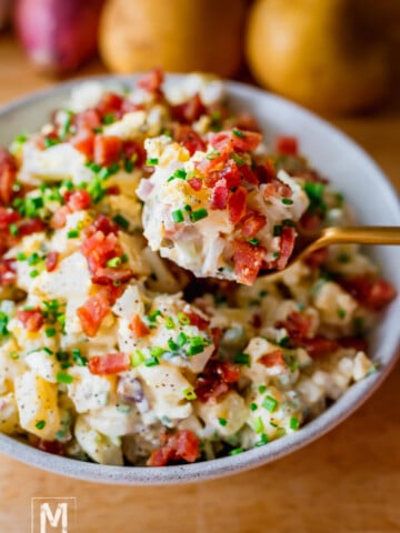 A bowl of Creamy Dill Pickle Potato Salad garnished with bacon pieces and chives.