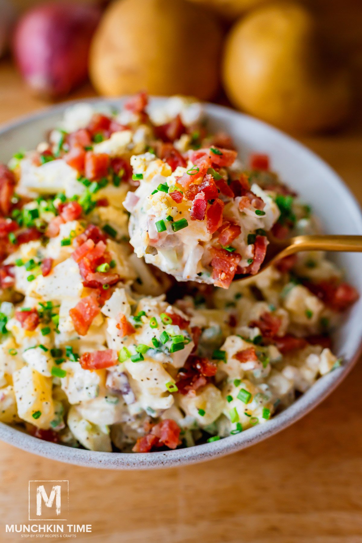 A bowl of Creamy Dill Pickle Potato Salad garnished with bacon pieces and chives.