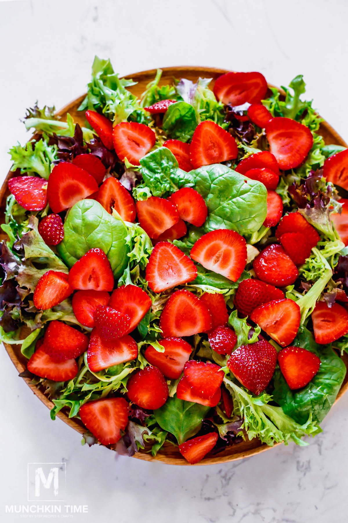 delicious sliced strawberries added to the spinach and other greens on a plate.