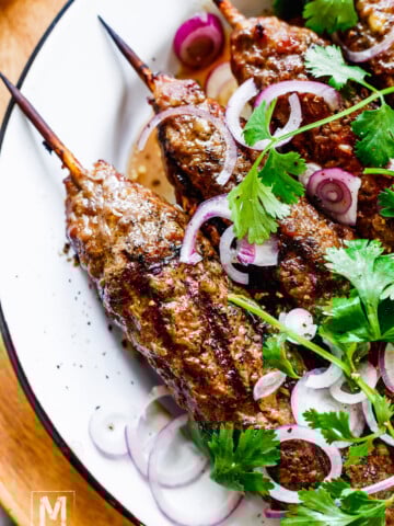 Georgian Ground Beef Kebabs on a plate garnished with red onion and cilantro.