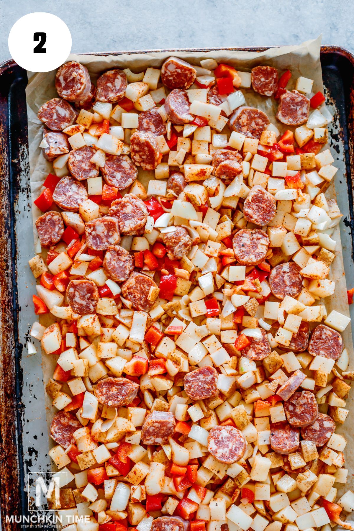 seasoned potatoes, sausages, peppers, and onions on a large sheet pan.