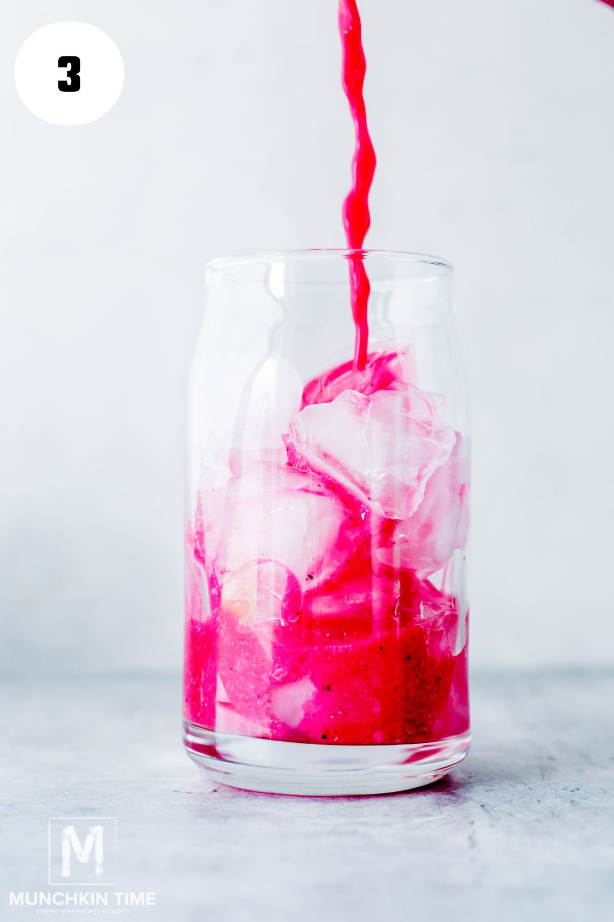 tall glass with ice being filled with blended mango and dragon fruit mixture.
