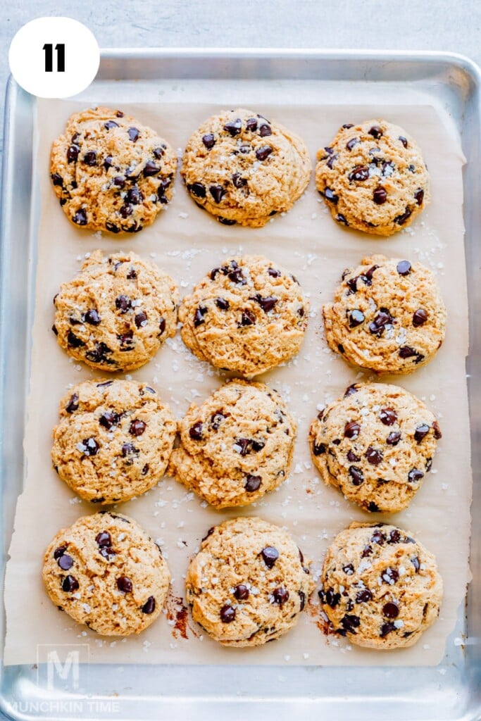 A baking sheet with 12 freshly baked sourdough chocolate chip cookies on parchment paper, viewed from above.